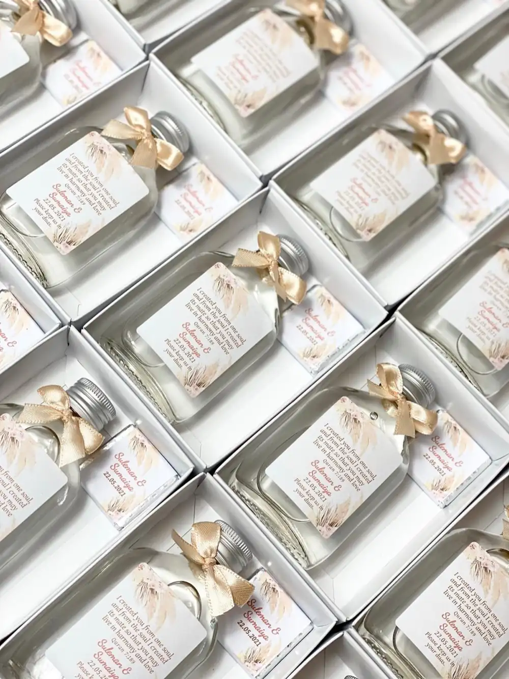 Rows of white gift boxes each holding a labelled glass bottle with a satin ribbon and a wrapped chocolate
