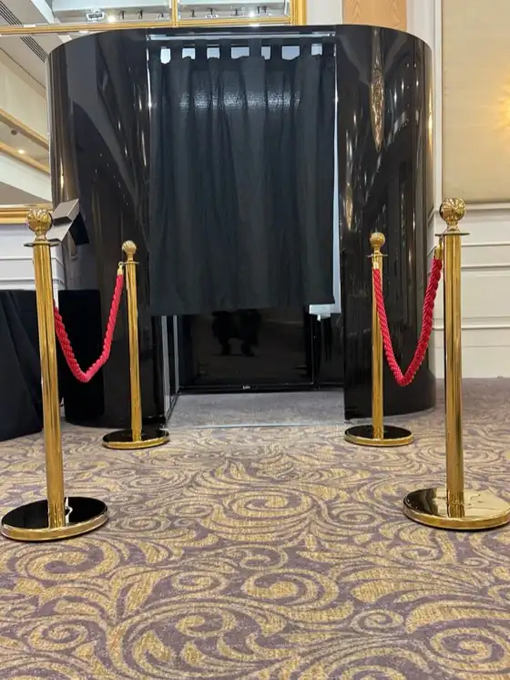 Black enclosed photo booth with gold posts and red ropes